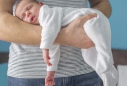 Baby sleeping in a position on his father’s arm to help treat colic