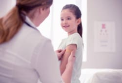 Dark-haired doctor wearing white jacket puts bandage on girl's arm
