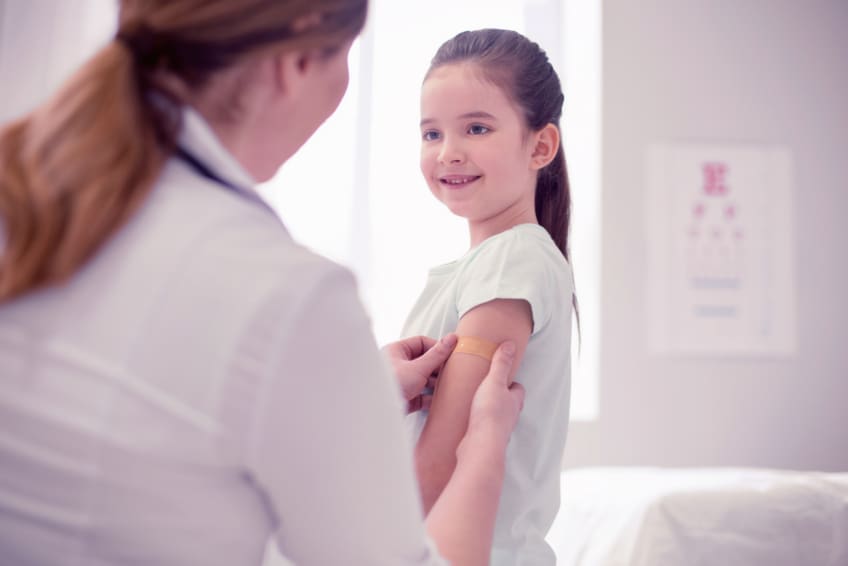 Dark-haired doctor wearing white jacket puts bandage on girl's arm