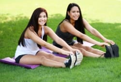 Two women sitting in grass stretching before exercising