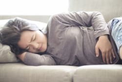 A woman who suffering from cramps is lying on the sofa with her hand on her abdomen.