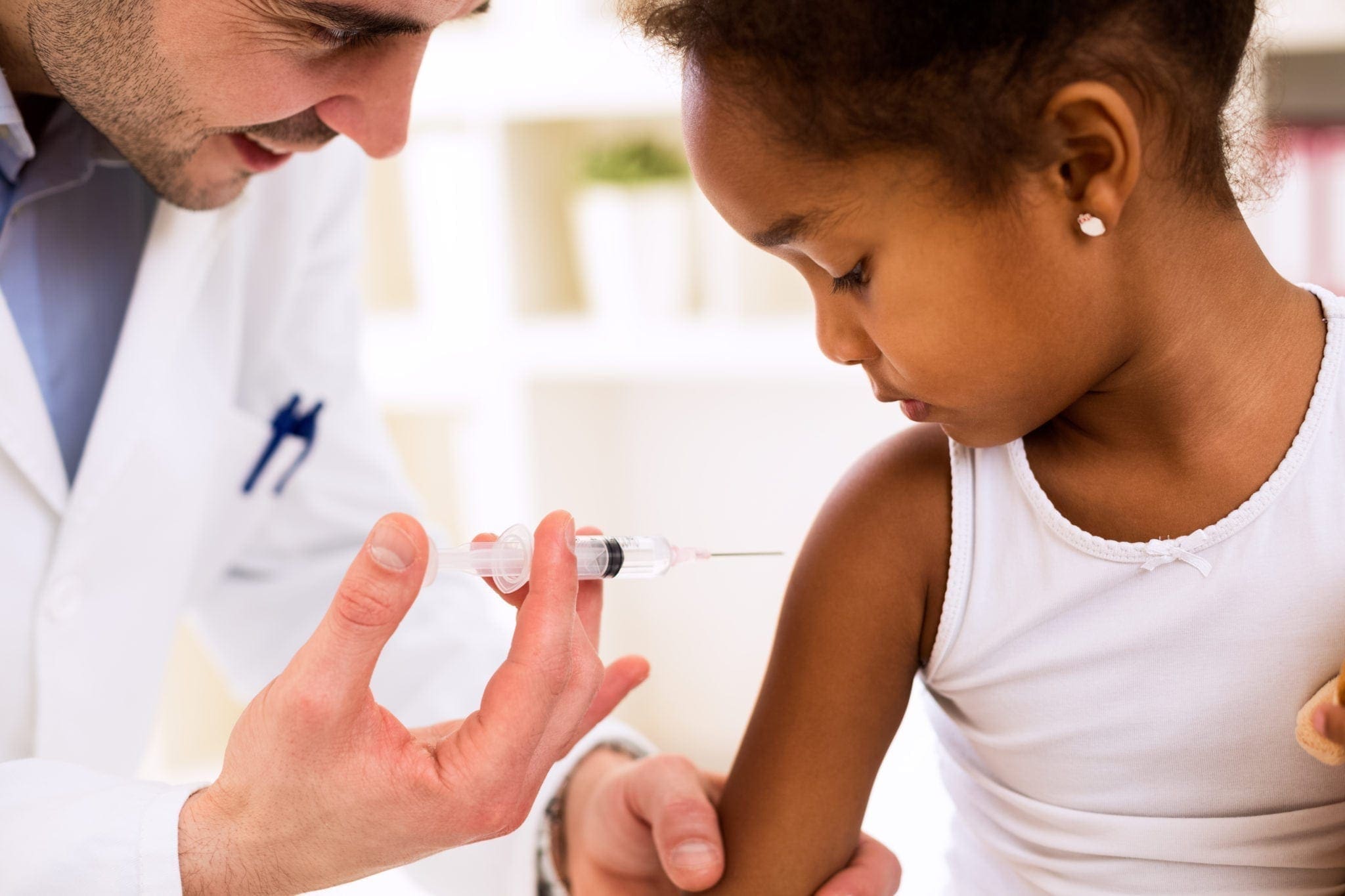  A smiling doctor is giving a vaccination to a young girl who is looking away with no reaction.