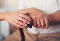 close-up of an elderly man’s hands on top of a cane with a caregiver’s hand on top