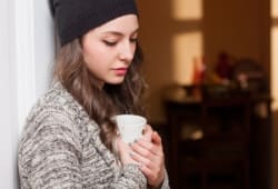 sad-looking young woman looks down over a mug of hot beverage