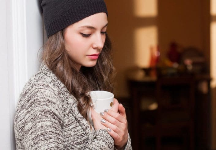 sad-looking young woman looks down over a mug of hot beverage