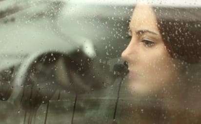 A young woman with depression looks out her car window on a rainy day.