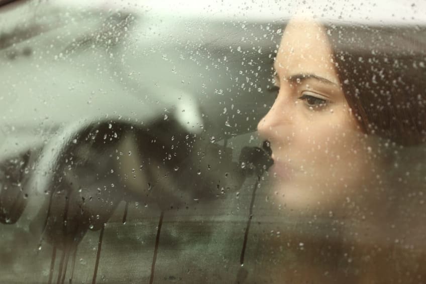 A young woman with depression looks out her car window on a rainy day.