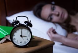 woman lying in bed stares at clock in the middle of the night