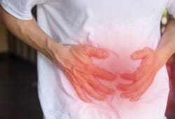 Man's hands on his stomach with red spot indicating pain caused by irritable bowel syndrome (IBS)