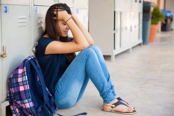 stressed teenager sitting against lockers in school