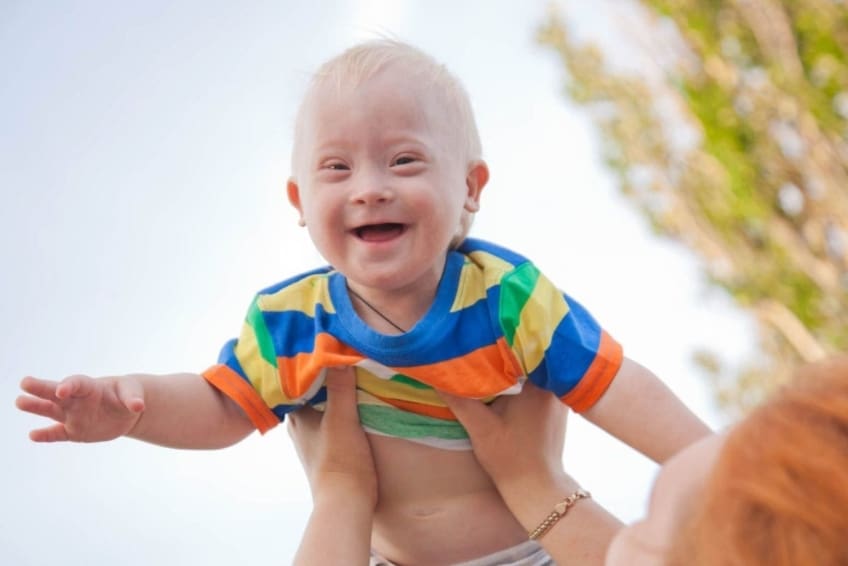 Portrait of a baby with Down syndrome. A mother picking up her son, the child is happy and flying up