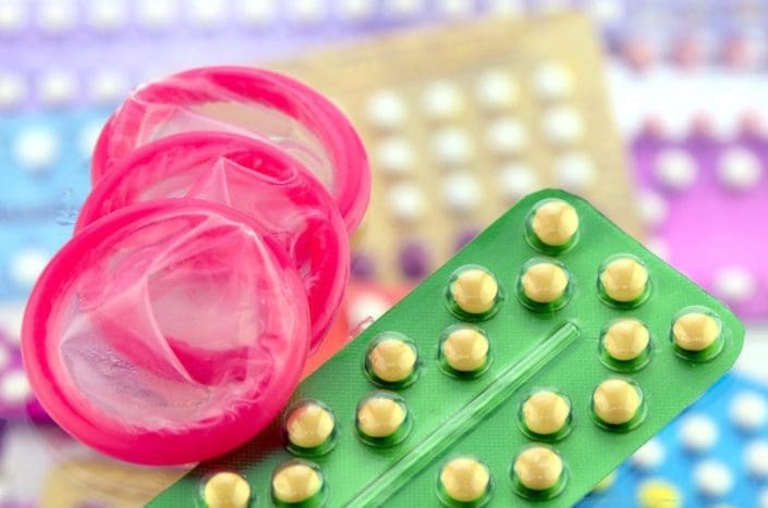 Condom and oral contraceptive pill on pharmacy counter with colorful pills strips background.