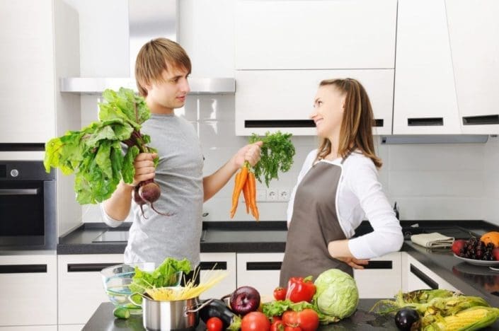 Two family members in the kitchen cooking a meal with lots of vegetables