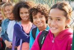 Smiling school children stand against a fence on the playground. Tourette syndrome is a movement disorder that causes a person to make repeated, uncontrolled twitches, movements, or sounds known as tics.