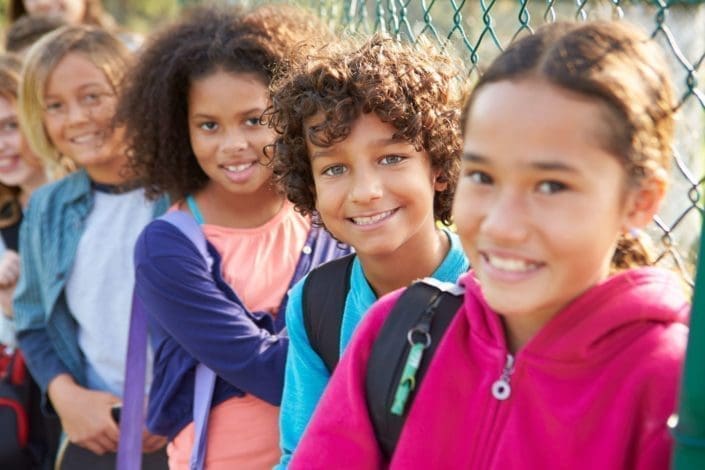 smiling school children stand against a fence on the playground