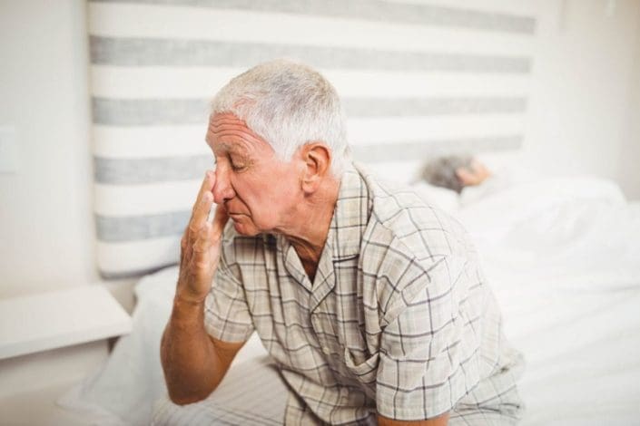 Older man, who canâ€™t sleep at night, sitting on bed while spouse sleeps