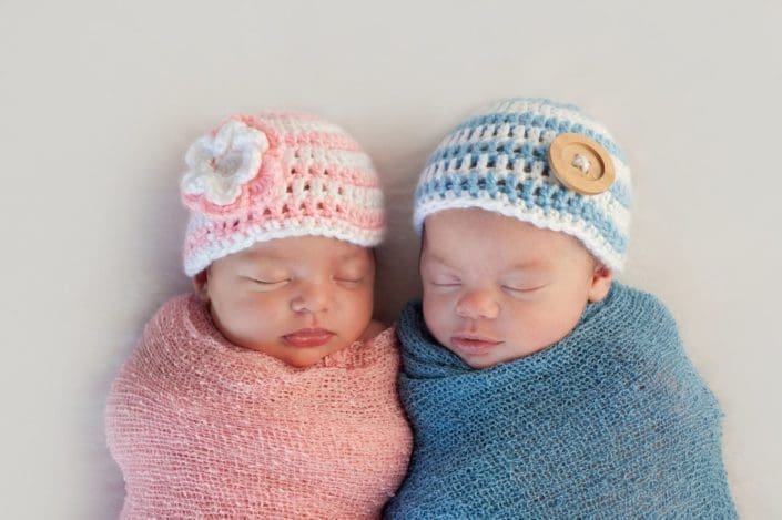 A baby girl wrapped in a pink blanket laying next to her baby brother wrapped in a blue blanket