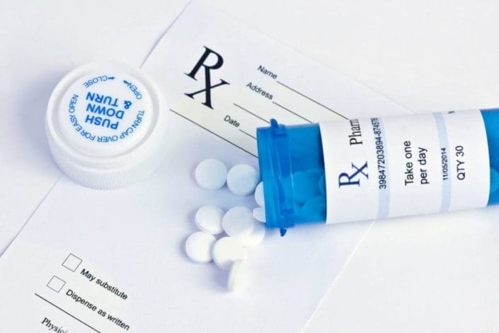 bottle of white pills spilled on top of prescription pad