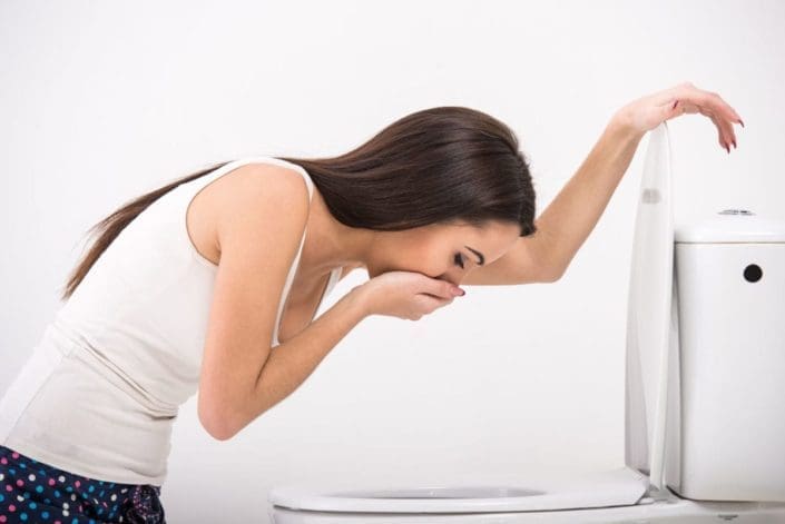 A young woman leans over a toilet bowl as if she may vomit. Morning sickness refers to the nausea and vomiting some people have when they become pregnant. It affects the majority of pregnant people.