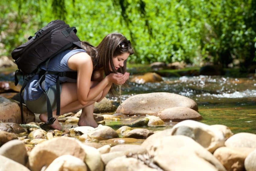 Young woman drinking from stream