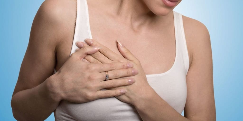 Close-up cropped portrait of young woman with breast pain touching chest