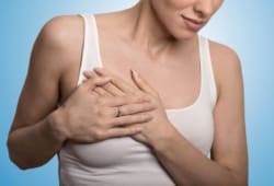 Close-up cropped portrait of young woman with breast pain touching chest