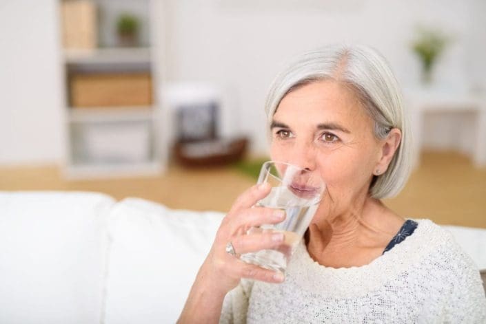 Middle-aged woman drinking a glass of water in the living room and looking into the distance