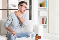 Man sitting on sofa, holding shoulder in pain