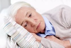 Elderly, depressed woman lying on pillow