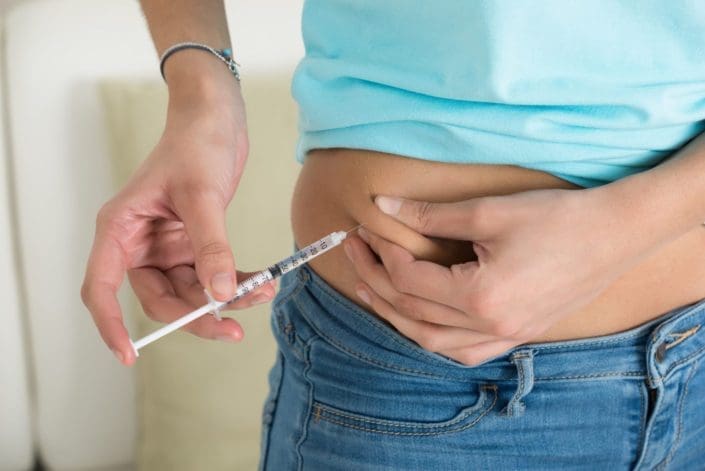 A woman injecting insulin into her stomach at home