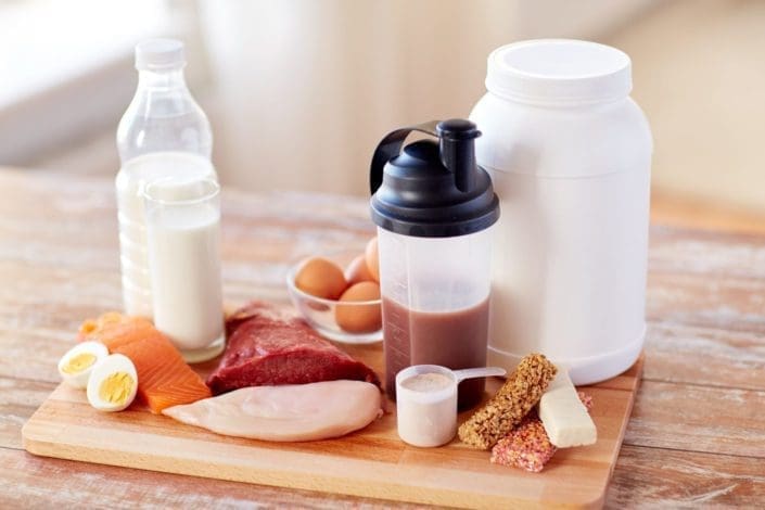 Lots of healthy proteins and protein drinks sitting on a wooden cutting board