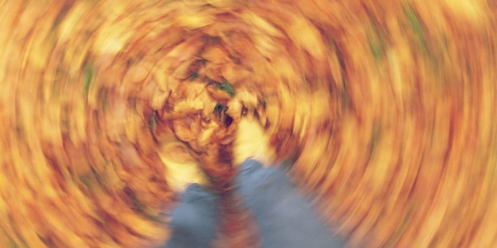 blurred, spinning picture of a person’s feet as they walk through fall leaves