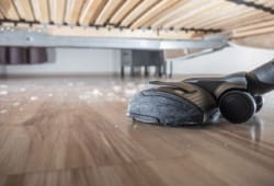 a vacuum sucks up dust on a hardwood floor under a bed