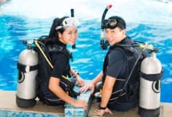 Woman and man in wet suits with oxygen tanks, learning how to safely scuba dive