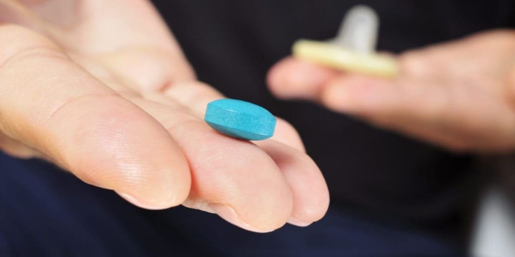 Man holding condom in one hand and blue pill in the other
