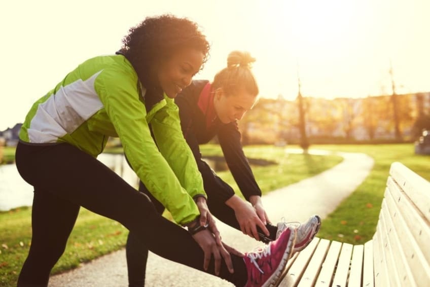 Two young women doing leg safety stretches before running in park
