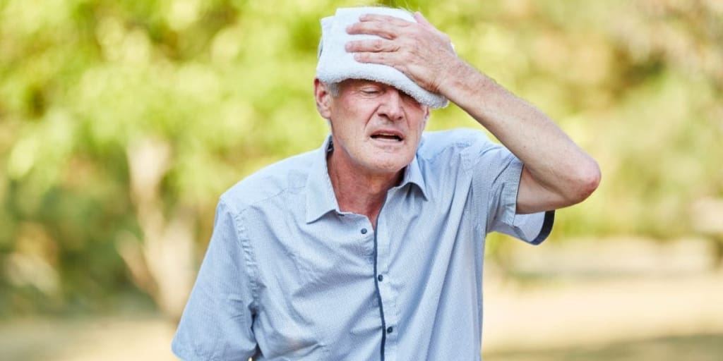 Senior man with heat exhaustion cools his head with a wet cold cloth
