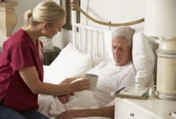 Nurse providing care to elderly man at home in bed