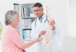 doctor and senior female patient look at a model of a spine