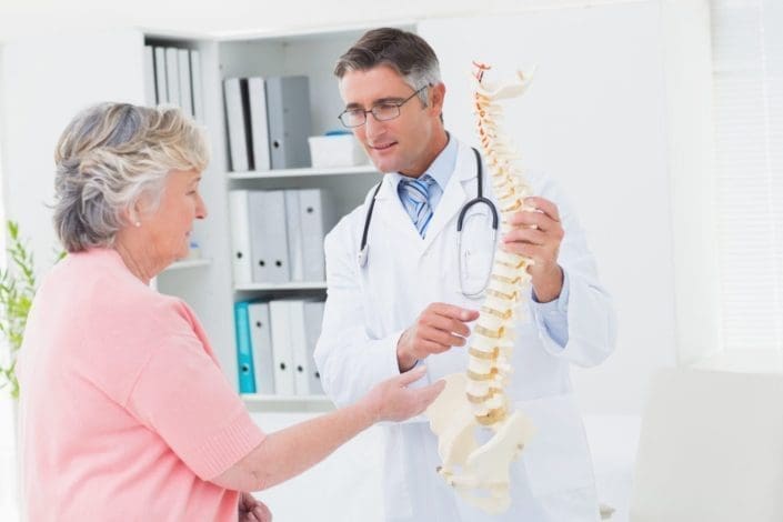 doctor and senior female patient look at a model of a spine