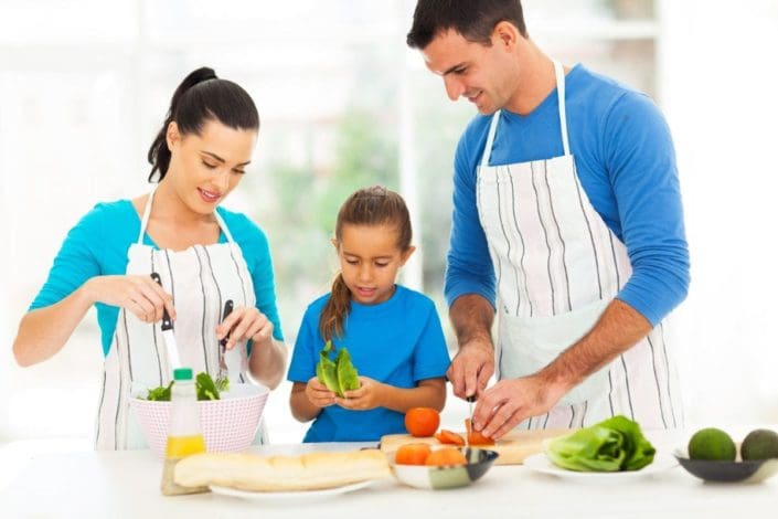 Parents and young child prepare healthy meal together in kitchen
