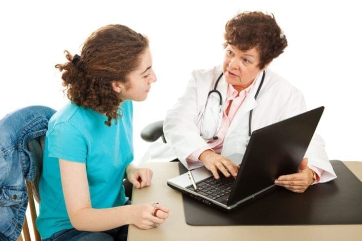 doctor with laptop counsels a young female patient at a desk