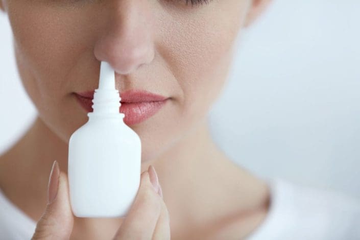 Young woman holding nose spray near her nose, ready to use it