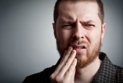 A man holds his mouth in pain. Burning mouth syndrome (BMS) is marked by pain and discomfort in the mouth, lips, and/or tongue.