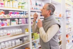 sick man holding tissue looks at OTC decongestants in a pharmacy