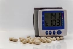 blood pressure monitor showing elevated readings with pills on a table