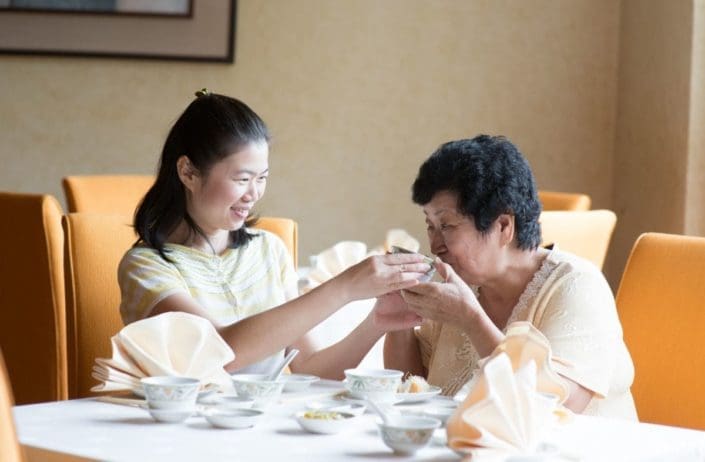 young woman helps older woman hold her tea cup as she takes a drink