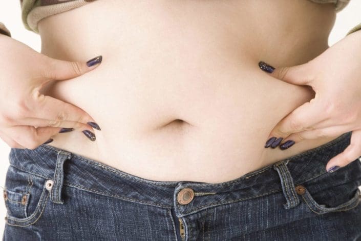 A close-up of a woman pinching fat on her stomach