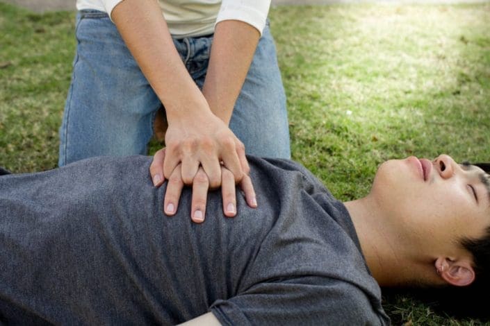 Young man lying on grass while female bends over him doing CPR