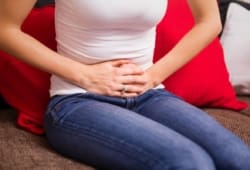 Woman suffering from menstrual cramps holds her stomach while sitting on couch. Dysmenorrhea is the medical term for pain that women have before or during menses (known as their period). It usually is not serious.